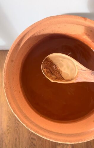 A Wooden Ladle Scoops Water from.a Miriam's Pure Clay Water Jar